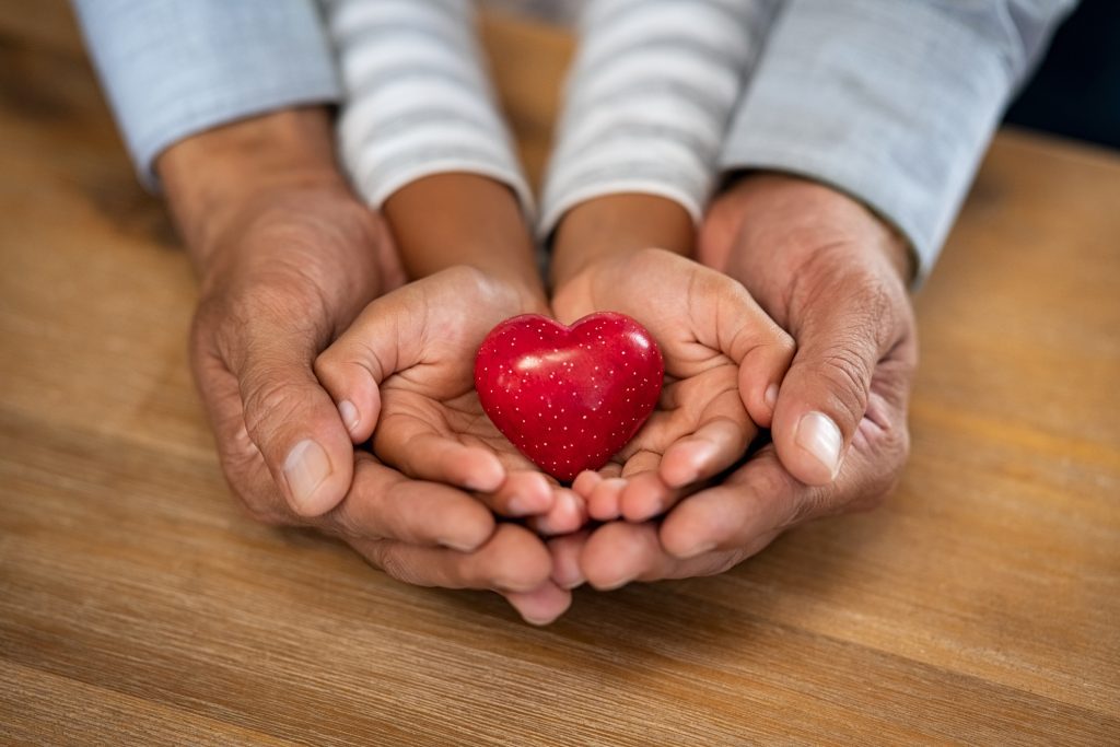 Man and child hand holding red heart stone